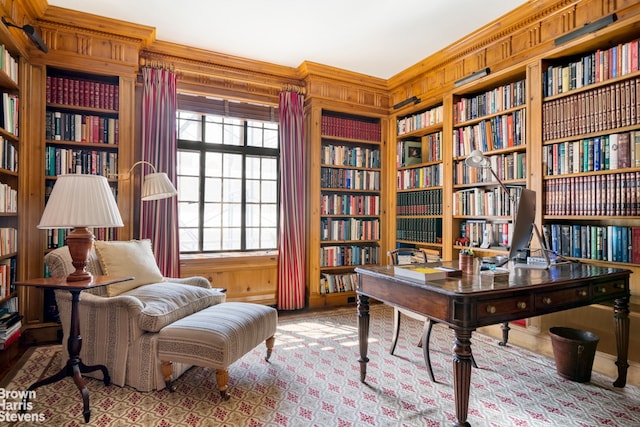 home office featuring wall of books, wooden walls, built in shelves, and crown molding