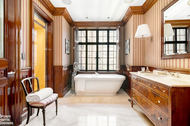 bathroom featuring wallpapered walls, a soaking tub, crown molding, wainscoting, and vanity