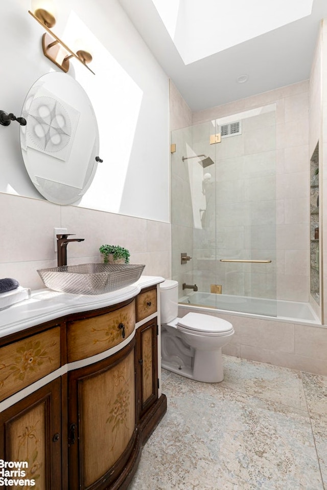 bathroom featuring toilet, tile walls, a skylight, vanity, and tiled shower / bath