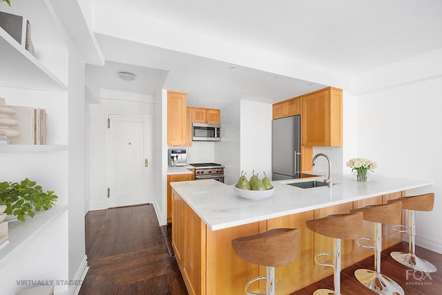 kitchen featuring high quality appliances, a sink, a peninsula, dark wood-type flooring, and baseboards