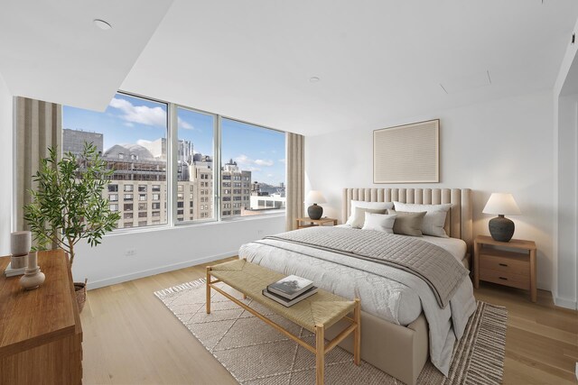 bedroom featuring light wood finished floors, baseboards, and a view of city