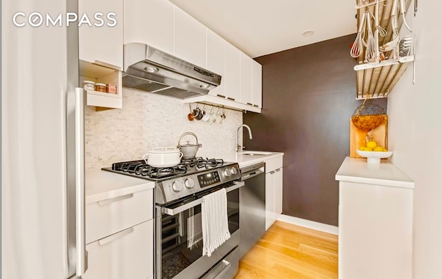 15 Charles St Unit 6G, New York City, NY 10014 - kitchen featuring appliances with stainless steel finishes, under cabinet range hood, a sink, light wood-style flooring, and white cabinets