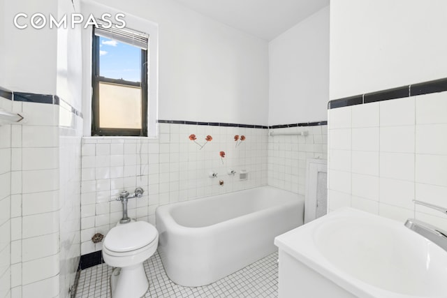 bathroom featuring tile walls, a garden tub, toilet, tile patterned floors, and wainscoting