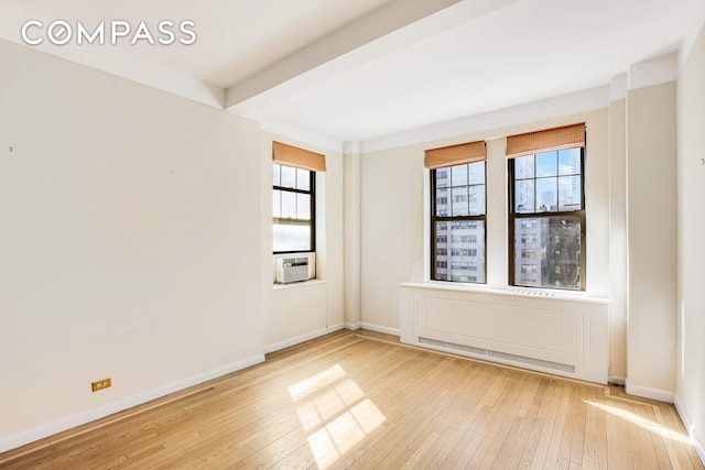empty room with light wood-style floors, baseboards, beamed ceiling, and cooling unit