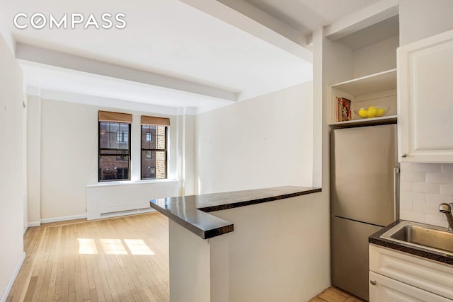 kitchen featuring dark countertops, a sink, freestanding refrigerator, light wood-style flooring, and a peninsula