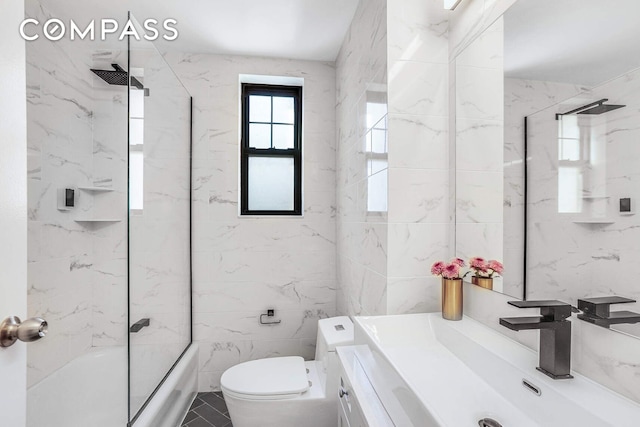 bathroom with toilet, vanity, tile walls, and bath / shower combo with glass door
