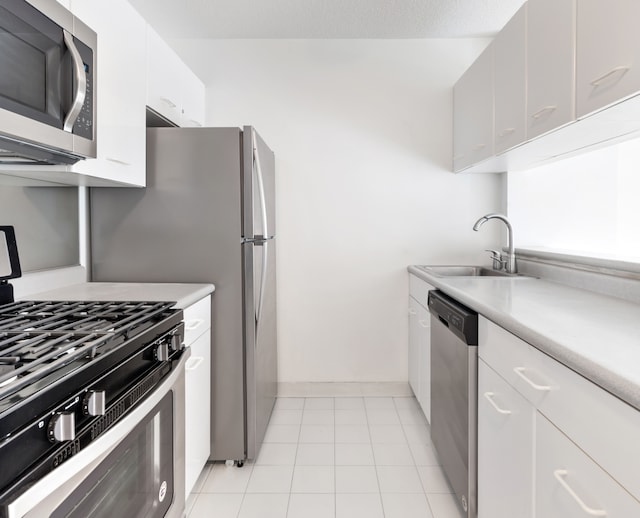 kitchen featuring appliances with stainless steel finishes, a sink, white cabinets, light countertops, and baseboards