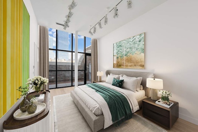 bedroom featuring a wall of windows, track lighting, baseboards, and wood finished floors