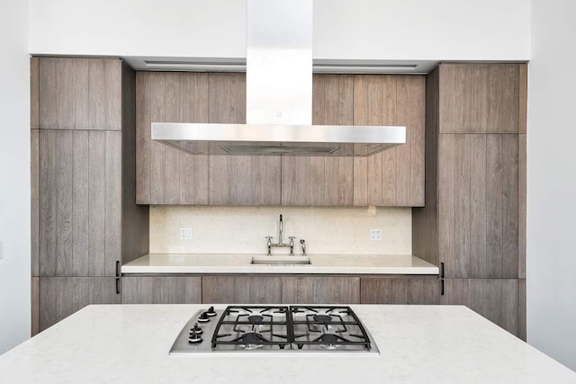 kitchen featuring wall chimney range hood, modern cabinets, stainless steel gas cooktop, a sink, and light countertops