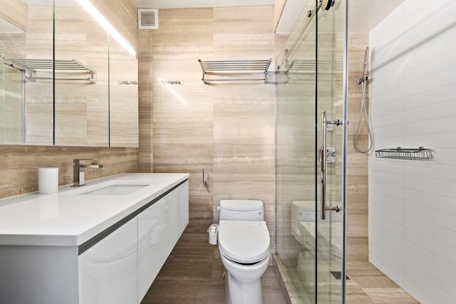 full bath with toilet, visible vents, a shower stall, and tile walls