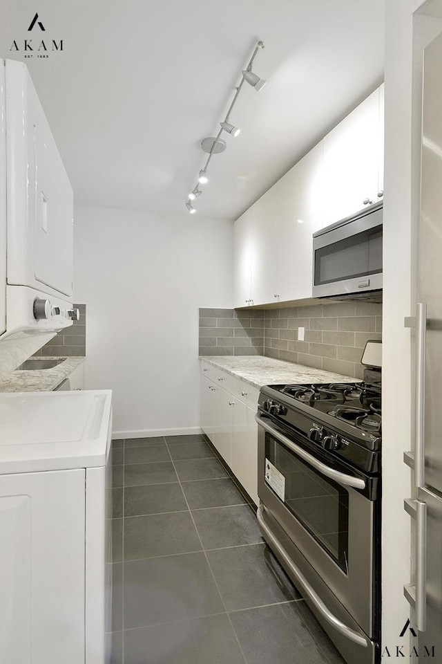 kitchen featuring tasteful backsplash, stacked washing maching and dryer, track lighting, white cabinetry, and appliances with stainless steel finishes