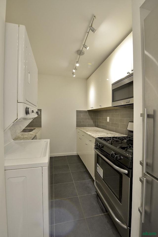 343 E 74th St Unit 7-J, New York City, NY 10021 - kitchen featuring stainless steel appliances, stacked washer / dryer, rail lighting, dark tile patterned flooring, and white cabinets