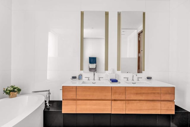 full bath featuring a sink, a freestanding bath, tile walls, and double vanity
