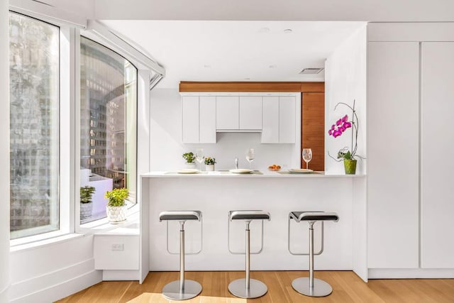 kitchen with a wealth of natural light, white cabinets, a kitchen bar, and light countertops