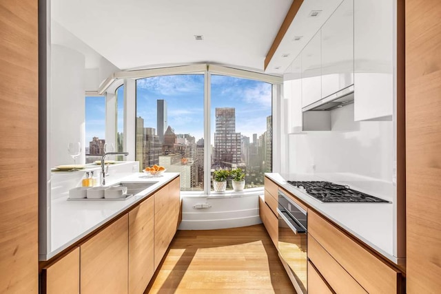 kitchen with gas cooktop, a sink, wall oven, white cabinetry, and a view of city