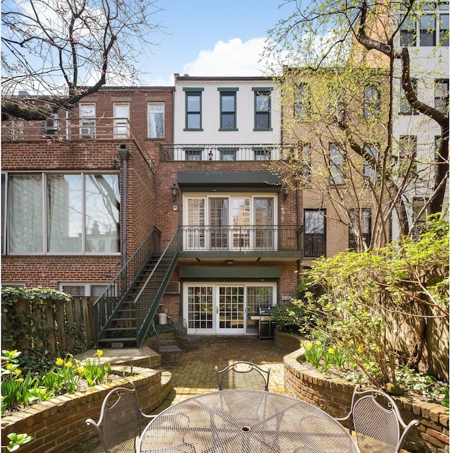 rear view of house featuring brick siding, a patio, outdoor dining area, and stairway