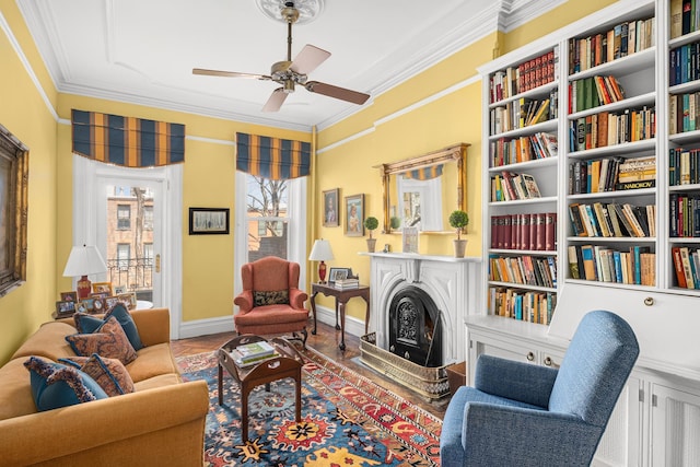 sitting room with wood finished floors, ornamental molding, baseboards, a fireplace, and ceiling fan