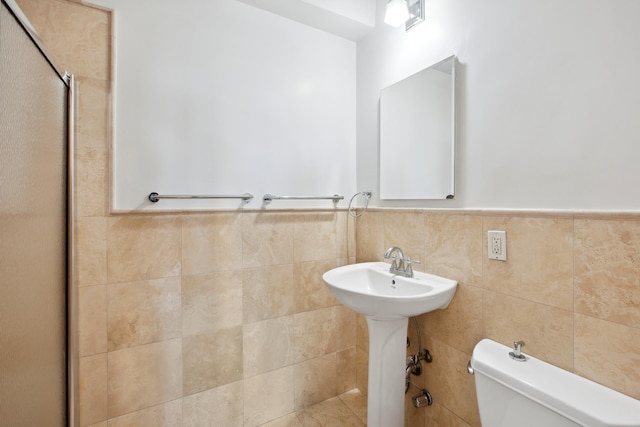 bathroom with toilet, tile walls, a wainscoted wall, and a sink