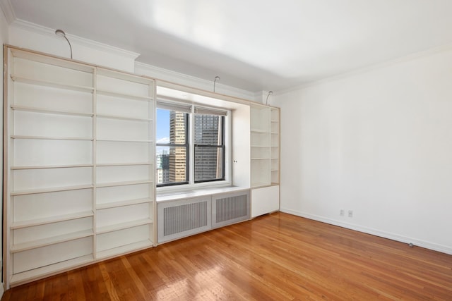 empty room with ornamental molding, wood finished floors, radiator heating unit, and baseboards