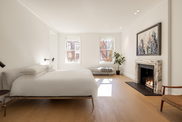 bedroom with light wood-style floors, ornamental molding, baseboards, and a high end fireplace
