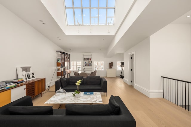 living area with light wood-type flooring, a high ceiling, a skylight, and baseboards