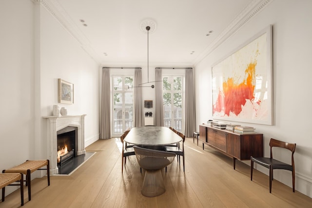 dining area featuring a fireplace with flush hearth, baseboards, crown molding, and light wood-type flooring