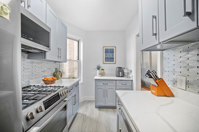 601 E 19th St Unit 2M, New York City, NY 11226 - kitchen with appliances with stainless steel finishes, light stone countertops, tasteful backsplash, gray cabinetry, and light wood finished floors