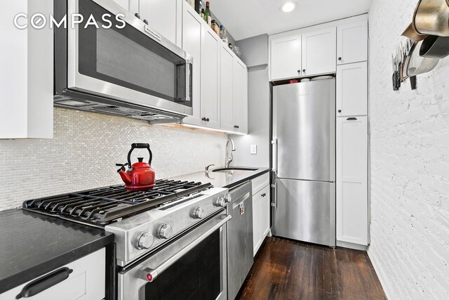 458 W 23rd St Unit 3A, New York City, NY 10011 - kitchen featuring appliances with stainless steel finishes, dark wood-style floors, a sink, dark countertops, and white cabinetry