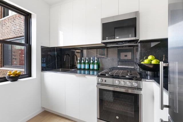 201 W 21st St Unit 11K, New York City, NY 10011 - kitchen with stainless steel appliances, modern cabinets, white cabinets, decorative backsplash, and light wood-style floors