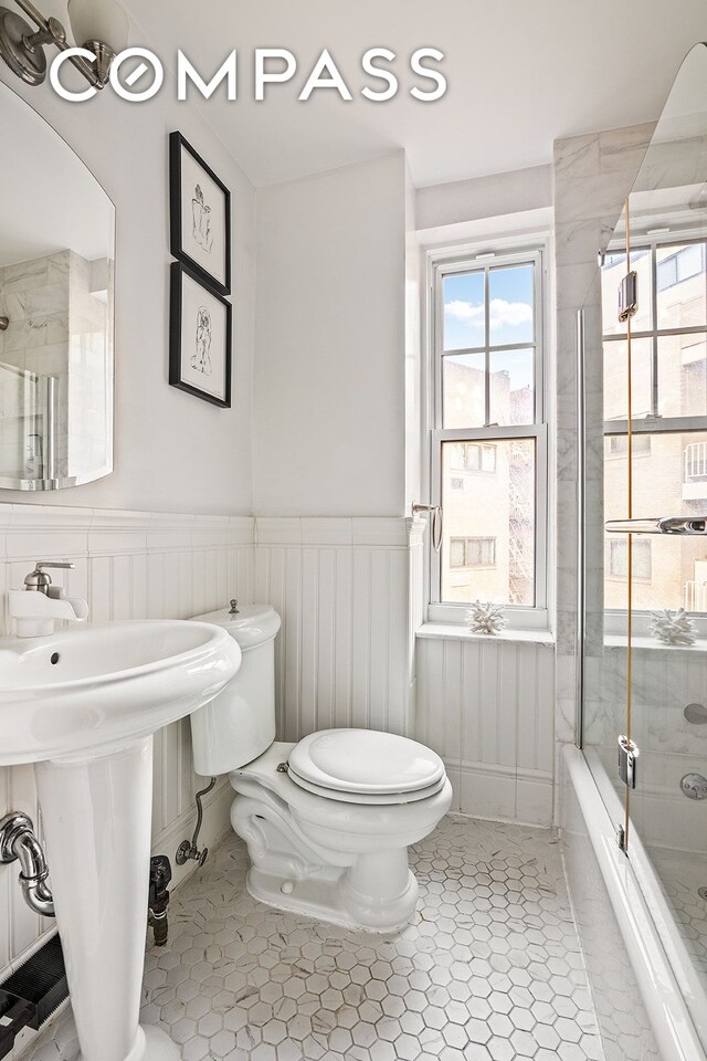 302 W 12th St Unit 5G, New York City, NY 10014 - bathroom with tile patterned flooring, wainscoting, a sink, combined bath / shower with glass door, and toilet