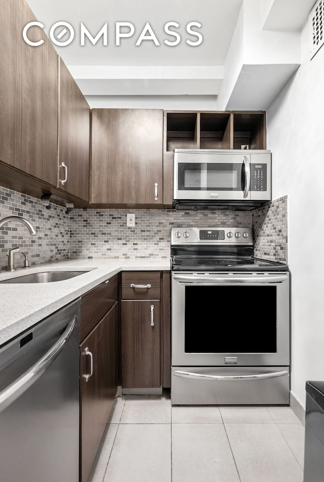 kitchen featuring appliances with stainless steel finishes, a sink, dark brown cabinetry, light tile patterned flooring, and backsplash