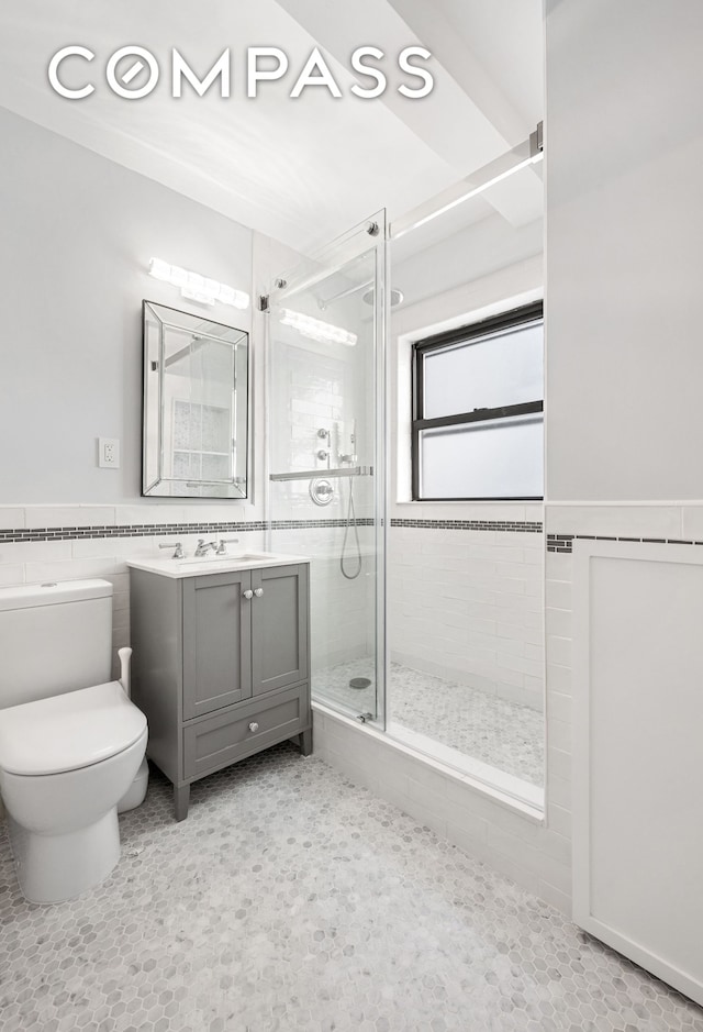 full bathroom with toilet, a shower stall, vanity, a wainscoted wall, and tile walls