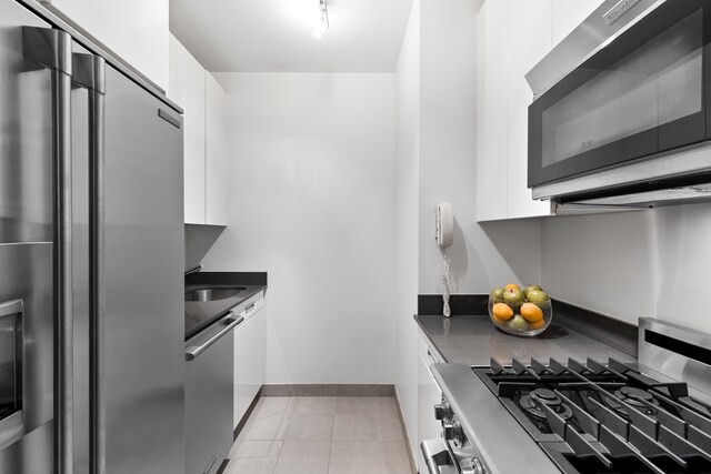 kitchen featuring appliances with stainless steel finishes, dark countertops, white cabinets, baseboards, and a sink