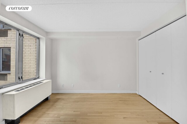 unfurnished bedroom with light wood finished floors, radiator, baseboards, and a closet