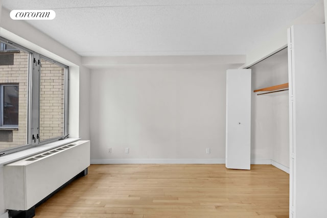 unfurnished bedroom with light wood-type flooring, a textured ceiling, baseboards, radiator heating unit, and a closet
