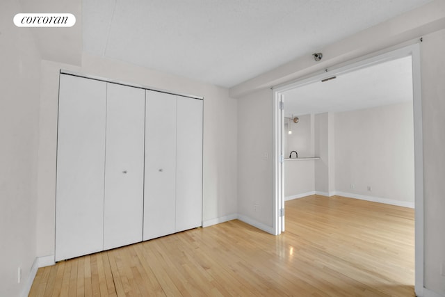 unfurnished bedroom with wood-type flooring, baseboards, and a closet