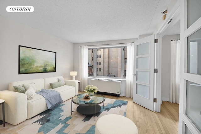 living room with a textured ceiling, light wood-style flooring, and radiator heating unit
