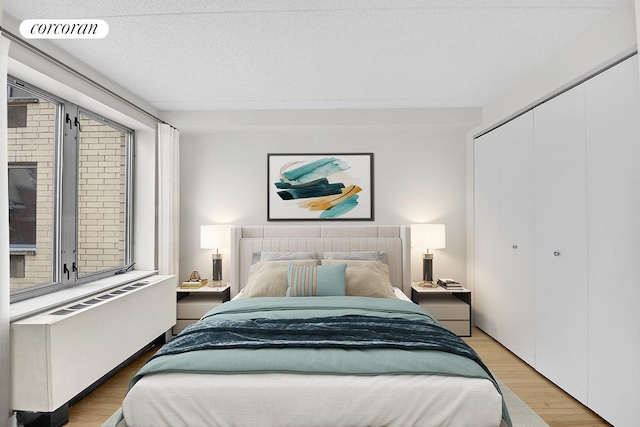 bedroom featuring radiator, light wood-type flooring, a closet, and a textured ceiling