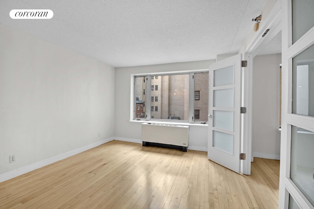 unfurnished room with radiator, light wood-style flooring, a textured ceiling, and baseboards