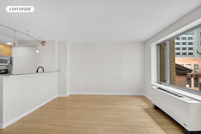 unfurnished living room with radiator heating unit, light wood-style flooring, a textured ceiling, and baseboards