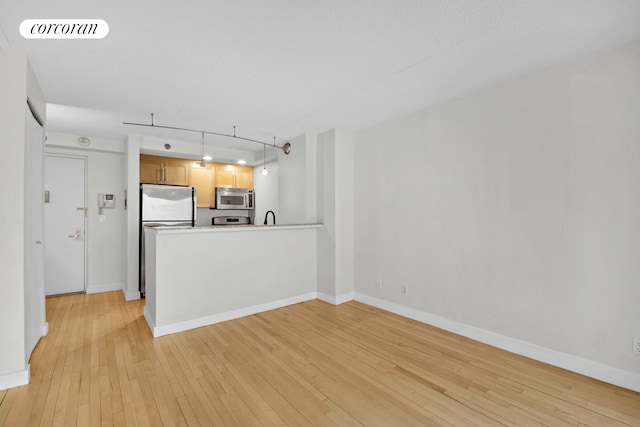 kitchen featuring stainless steel microwave, light wood finished floors, a peninsula, and baseboards