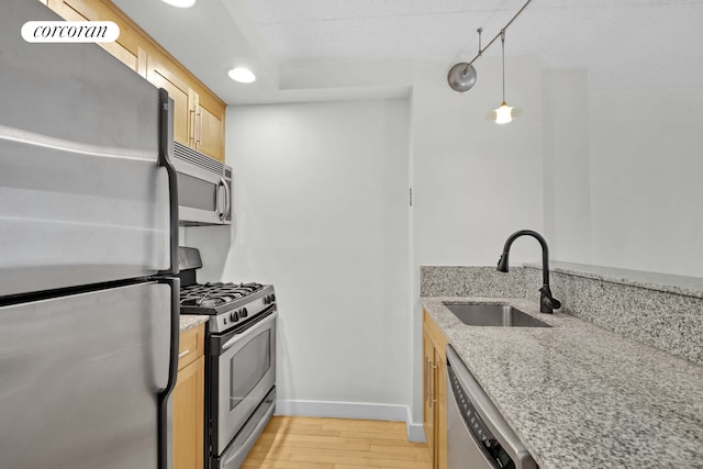 kitchen with appliances with stainless steel finishes, a sink, light brown cabinets, light wood-type flooring, and baseboards