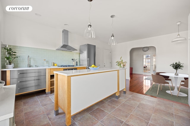 kitchen featuring arched walkways, wall chimney range hood, visible vents, appliances with stainless steel finishes, and light countertops