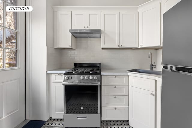 kitchen with freestanding refrigerator, stainless steel range with gas stovetop, under cabinet range hood, light countertops, and a sink