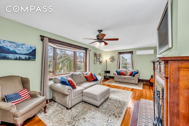 living room with a ceiling fan, a fireplace with flush hearth, wood finished floors, and a wall mounted air conditioner