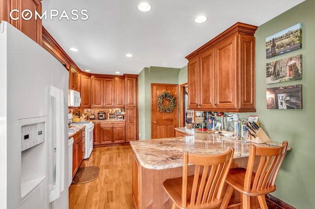 kitchen featuring light stone counters, a peninsula, light wood finished floors, recessed lighting, and white appliances