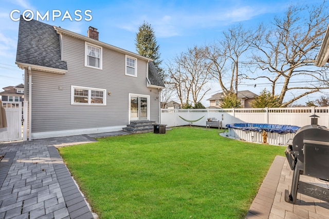 back of property featuring a fenced backyard, a chimney, a fenced in pool, a shingled roof, and a lawn