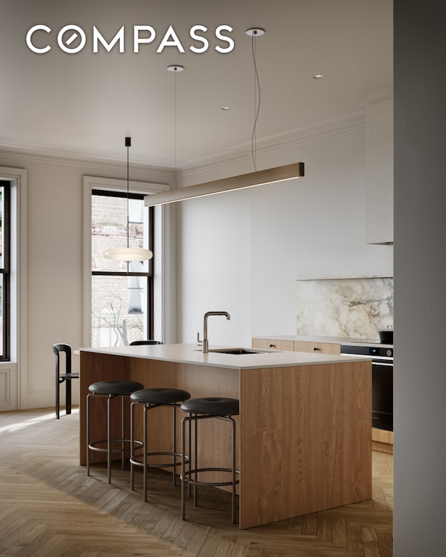 kitchen with ornamental molding, light countertops, a sink, a kitchen island with sink, and range
