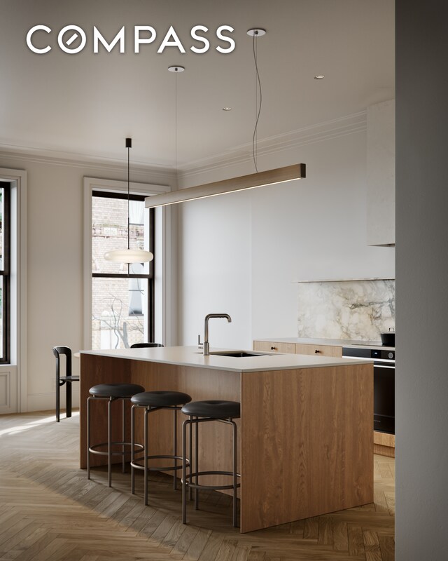 kitchen with crown molding, light countertops, a center island with sink, and a sink