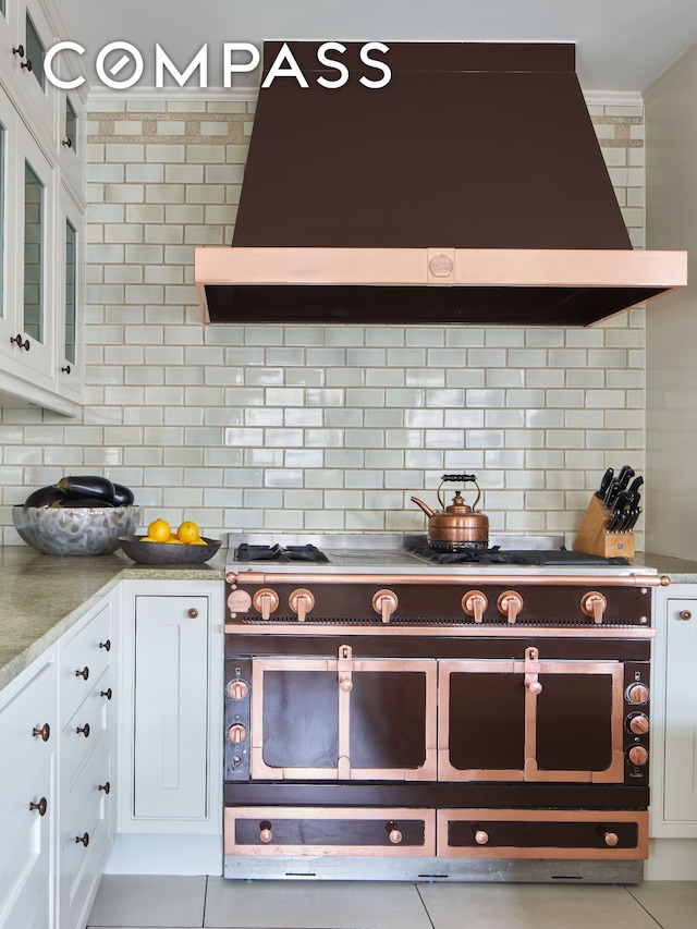 823 Park Ave Ph, Ph, New York City, NY 10021 - kitchen featuring wall chimney range hood, range with two ovens, backsplash, white cabinets, and ornamental molding